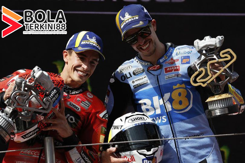 Marc Marquez dan Alex Marquez merayakan kemenangan di podium MotoGP Catalunya 2025 sambil mengangkat trofi juara, disorot oleh Bolaterkini88.